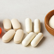 Verschiedene Vitamin-C-Präparate, darunter Acerola-Kirschen, Kapseln, Tabletten, Hagebutten und Fruchtpulver, auf einem hellen Hintergrund arrangiert.