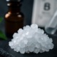 Makroaufnahme von weißen Borax-Kristallen vor einem Apothekerfläschchen und dem Elementsymbol für Bor – Symbolbild für naturheilkundliche Anwendung